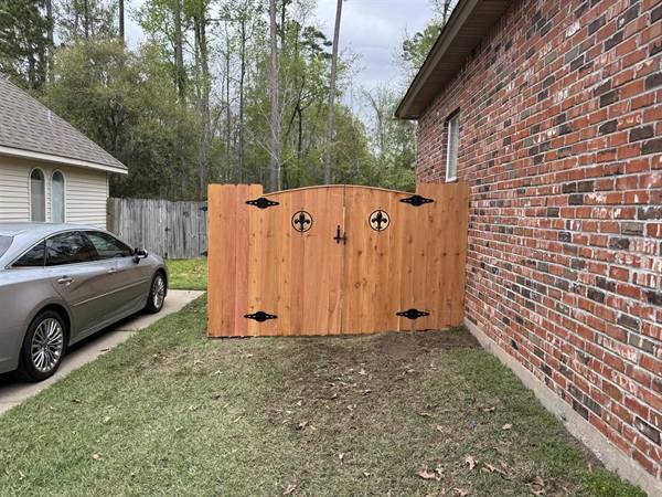 Arched cedar double gate with fleur-de-lis accents beside a brick home