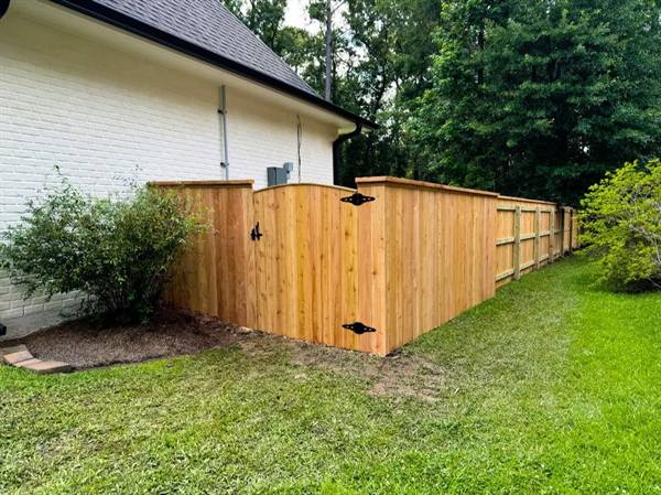 Cedar privacy fence and gate with top cap beside a white brick home