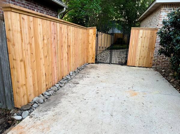 Capped cedar fence along a driveway with a wrought iron gate