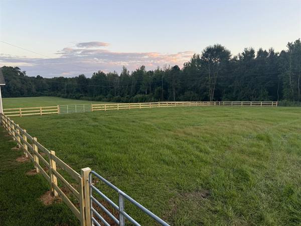 Three-rail wooden fence enclosing a pasture at dusk