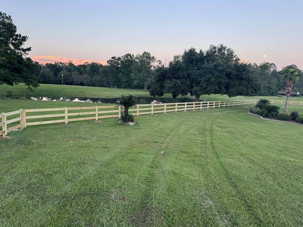 Three-rail ranch fence at sunset beside a pond