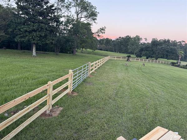 Three-rail fence with welded wire and a metal farm gate at dusk