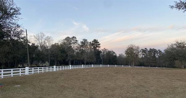 White three-rail fence curving around a pasture