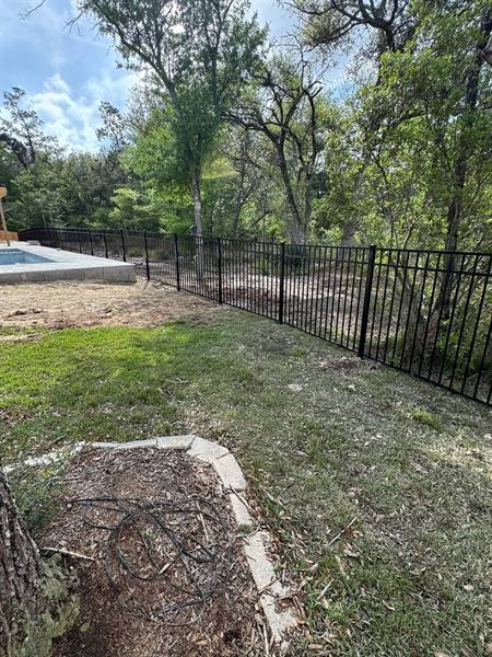 Black aluminum fence separating a pool area from the woods