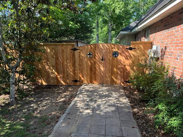 Arched cedar double gate with fleur-de-lis medallions and a paver walkway