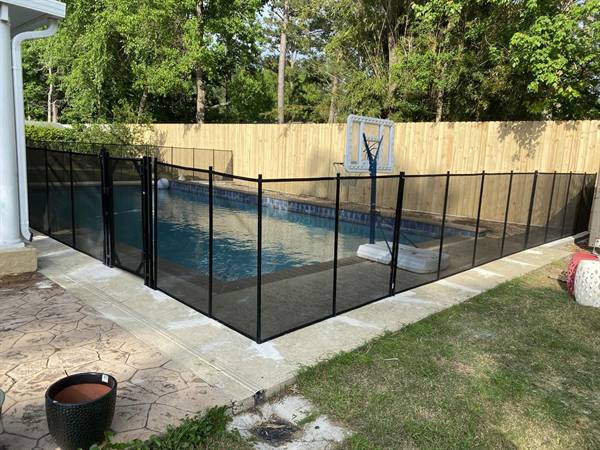 Black mesh pool safety fence around an in-ground pool