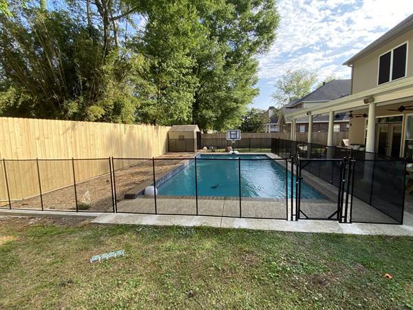 Removable black mesh pool safety fence around a backyard pool