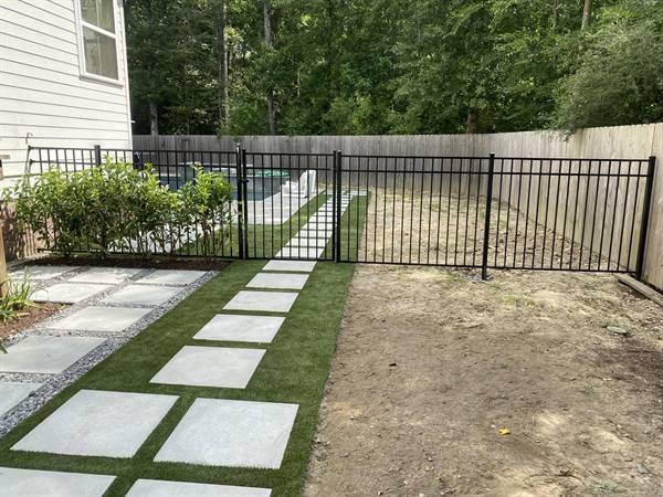 Black aluminum fence and gate beside a turf path to the pool