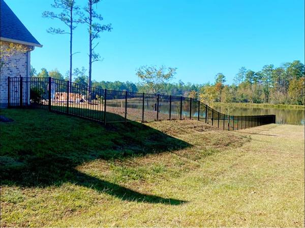 Black aluminum fence stepping down a slope toward a lake